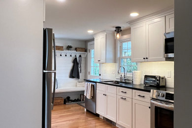 Inspiration for a small craftsman galley light wood floor and brown floor enclosed kitchen remodel in Bridgeport with an undermount sink, shaker cabinets, white cabinets, granite countertops, white backsplash, subway tile backsplash, stainless steel appliances, a peninsula and black countertops