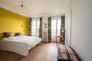 Exemple d'une grande chambre parentale tendance avec un mur jaune, parquet clair, aucune cheminée et un sol marron.