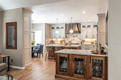 Photo of a medium sized classic l-shaped kitchen/diner in Denver with a submerged sink, beaded cabinets, beige cabinets, engineered stone countertops, white splashback, porcelain splashback, stainless steel appliances, medium hardwood flooring, multiple islands, brown floors and beige worktops.