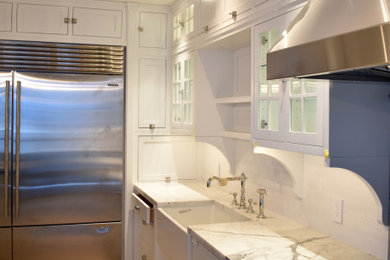 Large elegant u-shaped light wood floor and brown floor enclosed kitchen photo in Miami with a farmhouse sink, recessed-panel cabinets, white cabinets, marble countertops, subway tile backsplash, stainless steel appliances, an island and white countertops