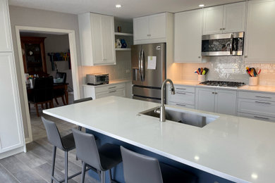 Kitchen pantry - mid-sized 1950s u-shaped light wood floor and gray floor kitchen pantry idea in Miami with an undermount sink, shaker cabinets, white cabinets, quartz countertops, white backsplash, subway tile backsplash, stainless steel appliances, a peninsula and white countertops