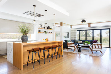 This is an example of a large contemporary l-shaped kitchen in Los Angeles with an undermount sink, flat-panel cabinets, grey cabinets, wood benchtops, white splashback, window splashback, stainless steel appliances, medium hardwood floors, with island, brown floor and brown benchtop.