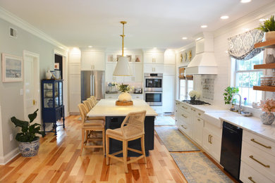 Example of a large french country l-shaped light wood floor and brown floor open concept kitchen design in Baltimore with a farmhouse sink, recessed-panel cabinets, white cabinets, quartz countertops, white backsplash, stainless steel appliances, an island and white countertops
