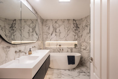 This is an example of a mid-sized contemporary bathroom in Sydney with flat-panel cabinets, dark wood cabinets, a freestanding tub, a corner shower, marble, white walls, marble floors, an integrated sink, solid surface benchtops, a hinged shower door, white benchtops, a niche, a double vanity and a floating vanity.