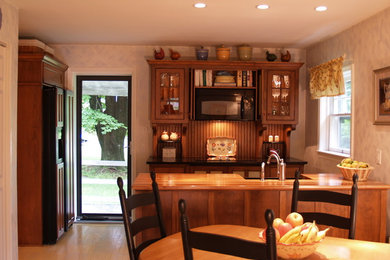 Open concept kitchen - small traditional galley light wood floor open concept kitchen idea in Philadelphia with a farmhouse sink, glass-front cabinets, medium tone wood cabinets, wood countertops, wood backsplash, paneled appliances and a peninsula