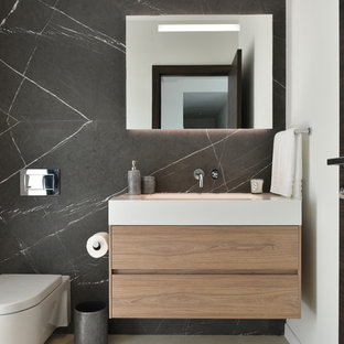 Trendy marble tile powder room photo in Miami with flat-panel cabinets, light wood cabinets, a wall-mount toilet, black walls, an integrated sink and white countertops