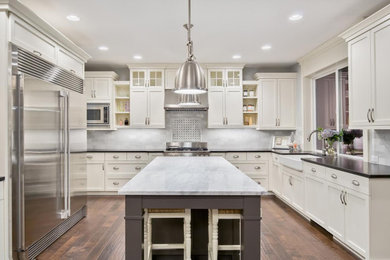 Inspiration for a large transitional u-shaped dark wood floor and brown floor eat-in kitchen remodel in Orange County with a farmhouse sink, recessed-panel cabinets, white cabinets, marble countertops, white backsplash, subway tile backsplash, stainless steel appliances, an island and white countertops