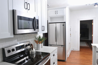 Example of a small danish galley medium tone wood floor and brown floor enclosed kitchen design in Oklahoma City with an undermount sink, shaker cabinets, white cabinets, quartzite countertops, white backsplash, ceramic backsplash, stainless steel appliances, an island and white countertops