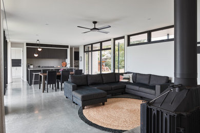 This is an example of a mid-sized contemporary open concept living room in Other with white walls, concrete floors, a wood stove, a wall-mounted tv and grey floor.