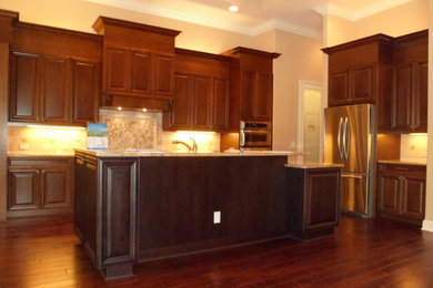 Mid-sized traditional l-shaped eat-in kitchen in Tampa with a double-bowl sink, raised-panel cabinets, dark wood cabinets, granite benchtops, beige splashback, ceramic splashback, stainless steel appliances, dark hardwood floors, with island and brown floor.