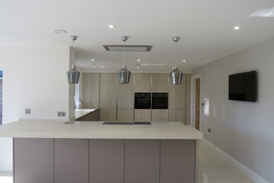 Photo of a large contemporary u-shaped open plan kitchen in Hertfordshire with an integrated sink, flat-panel cabinets, brown cabinets, quartz worktops, black appliances, porcelain flooring, no island, beige floors and white worktops.