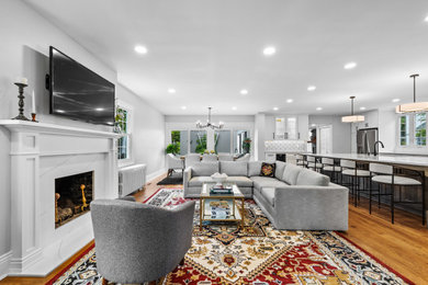 Example of a transitional medium tone wood floor and brown floor living room design in Baltimore with white walls, a standard fireplace and a wall-mounted tv