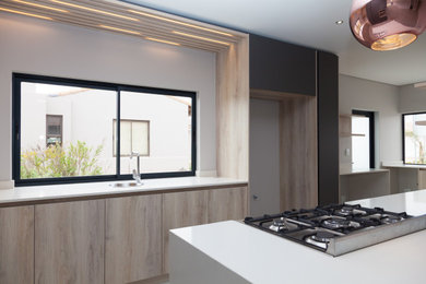 Example of a large minimalist l-shaped porcelain tile and gray floor open concept kitchen design in Other with a drop-in sink, flat-panel cabinets, light wood cabinets, quartz countertops, stainless steel appliances, an island and white countertops