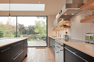 Design ideas for a mid-sized contemporary single-wall open plan kitchen in London with an undermount sink, flat-panel cabinets, blue cabinets, white splashback, porcelain splashback, stainless steel appliances, medium hardwood floors, with island and brown floor.
