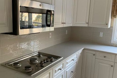 Transitional l-shaped kitchen photo in New York with raised-panel cabinets, white cabinets, beige backsplash and ceramic backsplash