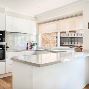 Design ideas for a mid-sized contemporary u-shaped kitchen pantry in Melbourne with a double-bowl sink, white cabinets, quartz benchtops, beige splashback, glass tile splashback, black appliances, vinyl floors, grey floor and beige benchtop.