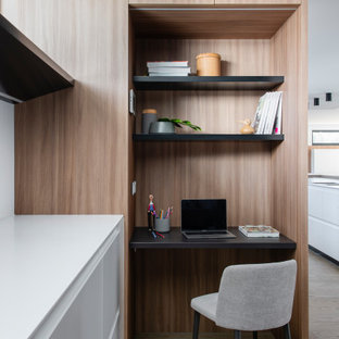 Photo of a large contemporary l-shaped kitchen pantry in Sydney with an undermount sink, flat-panel cabinets, solid surface benchtops, white splashback, black appliances, medium hardwood floors, with island and white benchtop.