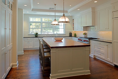 Kitchen pantry - large modern l-shaped medium tone wood floor and brown floor kitchen pantry idea in Philadelphia with a farmhouse sink, recessed-panel cabinets, white cabinets, white backsplash, subway tile backsplash, stainless steel appliances, an island and wood countertops