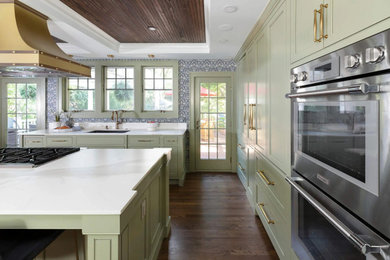 Example of a transitional medium tone wood floor, brown floor and tray ceiling open concept kitchen design in Detroit with an undermount sink, recessed-panel cabinets, green cabinets, quartz countertops, white backsplash, quartz backsplash, stainless steel appliances, an island and white countertops