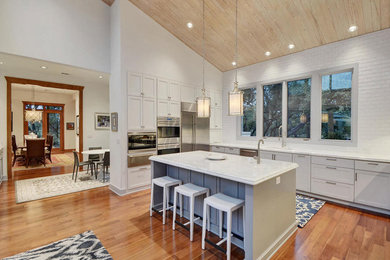 This is an example of a large transitional l-shaped eat-in kitchen in Austin with an undermount sink, shaker cabinets, white cabinets, marble benchtops, white splashback, subway tile splashback, stainless steel appliances, medium hardwood floors, with island and brown floor.