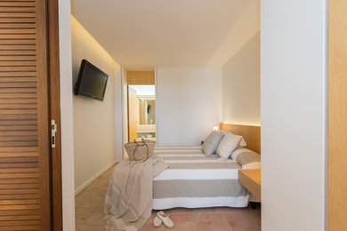 他の地域にある広い地中海スタイルのおしゃれな客用寝室 (テラコッタタイルの床、白い天井)