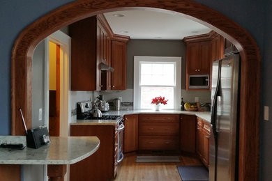 Eat-in kitchen - mid-sized traditional u-shaped medium tone wood floor eat-in kitchen idea in Other with shaker cabinets, medium tone wood cabinets, quartz countertops, gray backsplash, ceramic backsplash and stainless steel appliances
