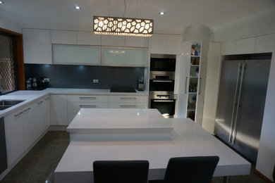 Modern eat-in kitchen in Brisbane with an undermount sink, white cabinets, brown splashback, glass sheet splashback, concrete floors and with island.
