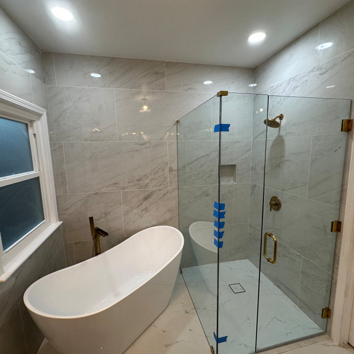 Marble-tiled bathroom with freestanding tub, glass shower enclosure, gold fixtures, and recessed lighting.