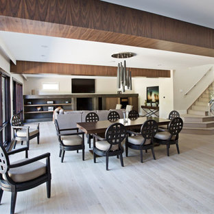 Immagine di una grande sala da pranzo aperta verso il soggiorno minimalista con pareti bianche, parquet chiaro, camino classico e cornice del camino in cemento
