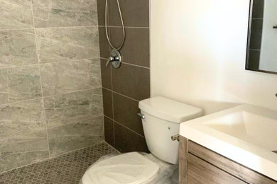 Example of a small 3/4 brown tile single-sink doorless shower design in Miami with furniture-like cabinets, medium tone wood cabinets, a one-piece toilet, white walls, white countertops and a freestanding vanity