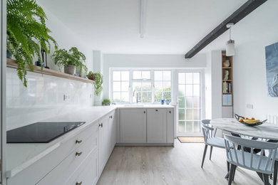 Inspiration for a medium sized classic enclosed kitchen in Oxfordshire with a single-bowl sink, recessed-panel cabinets, white cabinets, quartz worktops, white splashback, black appliances, light hardwood flooring, no island, beige floors and white worktops.