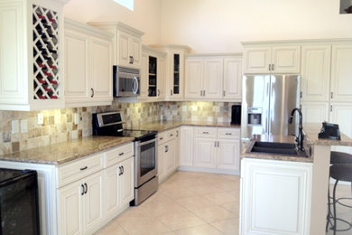Example of a large classic l-shaped porcelain tile and beige floor open concept kitchen design in Other with a double-bowl sink, raised-panel cabinets, red cabinets, granite countertops, beige backsplash, travertine backsplash, stainless steel appliances, an island and beige countertops