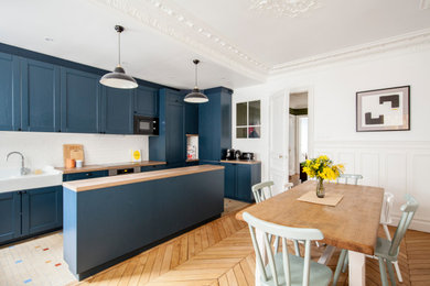 Photo of a large midcentury galley open plan kitchen in Paris with a single-bowl sink, blue cabinets, laminate countertops, white splashback, metro tiled splashback, black appliances, light hardwood flooring, an island and brown worktops.