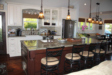 Mid-sized elegant l-shaped dark wood floor eat-in kitchen photo in Los Angeles with a farmhouse sink, raised-panel cabinets, white cabinets, granite countertops, brown backsplash, ceramic backsplash, stainless steel appliances and an island