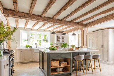 Inspiration for a large classic l-shaped enclosed kitchen in Surrey with a belfast sink, quartz worktops, mirror splashback, black appliances, limestone flooring, an island, white worktops and a chimney breast.
