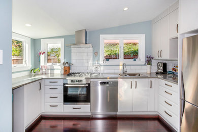 Photo of a small traditional u-shaped kitchen in Christchurch with a double-bowl sink, raised-panel cabinets, grey cabinets, quartz benchtops, white splashback, ceramic splashback, stainless steel appliances, painted wood floors, no island, red floor and grey benchtop.