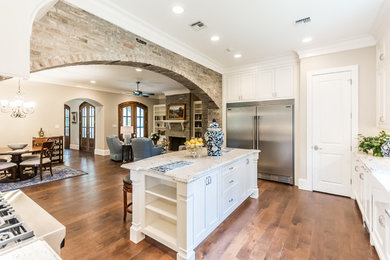 Example of a large classic l-shaped dark wood floor enclosed kitchen design in New Orleans with a farmhouse sink, shaker cabinets, white cabinets, granite countertops, white backsplash, subway tile backsplash, stainless steel appliances and an island