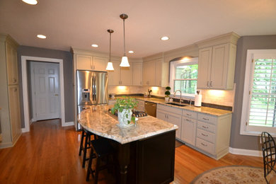 Inspiration for a large transitional u-shaped medium tone wood floor eat-in kitchen remodel in Columbus with an undermount sink, recessed-panel cabinets, white cabinets, granite countertops, beige backsplash, stone tile backsplash, stainless steel appliances and an island