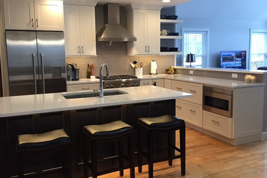 Open concept kitchen - transitional l-shaped light wood floor open concept kitchen idea in Other with recessed-panel cabinets, an island, an undermount sink, white cabinets, quartz countertops, gray backsplash, stainless steel appliances and ceramic backsplash