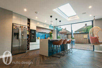 This is an example of a large modern single-wall open plan kitchen in London with a single-bowl sink, flat-panel cabinets, turquoise cabinets, quartz worktops, blue splashback, porcelain splashback, black appliances, medium hardwood flooring, an island, brown floors, white worktops, a drop ceiling and a feature wall.