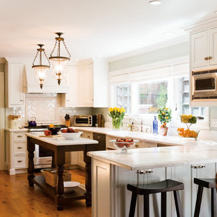 Réalisation d'une cuisine américaine tradition en U de taille moyenne avec une crédence en carreau de céramique, des portes de placard blanches, une crédence blanche, un électroménager en acier inoxydable, un plan de travail en marbre, un sol en bois brun, un îlot central, un évier de ferme et un placard à porte shaker.