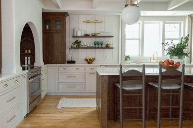 Transitional l-shaped medium tone wood floor, brown floor and exposed beam kitchen photo in Minneapolis with shaker cabinets, an undermount sink, gray cabinets, white backsplash, stainless steel appliances, an island and white countertops