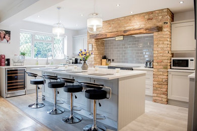 Design ideas for a mid-sized contemporary u-shaped kitchen in Hertfordshire with a farmhouse sink, recessed-panel cabinets, grey cabinets, quartzite benchtops, grey splashback, with island, white floor and subway tile splashback.