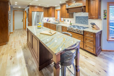 Photo of a small traditional l-shaped eat-in kitchen in Boston with an undermount sink, beaded inset cabinets, brown cabinets, granite benchtops, beige splashback, travertine splashback, stainless steel appliances, light hardwood floors, with island and beige floor.