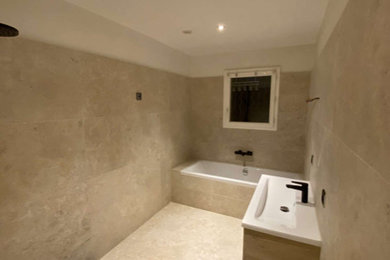 Inspiration pour une salle de bain minimaliste en bois clair avec une baignoire posée, une douche à l'italienne, un carrelage beige, un carrelage de pierre, un plan vasque, une cabine de douche à porte battante et meuble simple vasque.