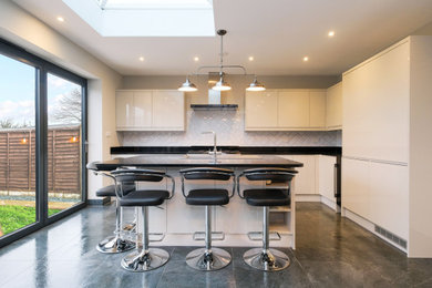 This is an example of a medium sized contemporary kitchen/diner in Essex with a built-in sink, flat-panel cabinets, white cabinets, granite worktops, black splashback, granite splashback, integrated appliances, porcelain flooring, an island, grey floors and black worktops.