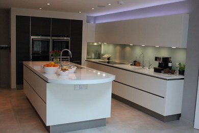 Medium sized contemporary l-shaped kitchen/diner in Surrey with flat-panel cabinets, white cabinets, quartz worktops, green splashback, glass sheet splashback, stainless steel appliances and an island.