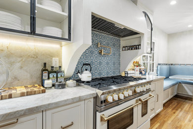 Example of a mid-sized tuscan light wood floor kitchen pantry design in Los Angeles with glass-front cabinets, white cabinets, quartzite countertops, blue backsplash, ceramic backsplash, white appliances, an island and a farmhouse sink
