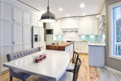 Inspiration for a mid-sized transitional l-shaped light wood floor open concept kitchen remodel in Other with an undermount sink, recessed-panel cabinets, white cabinets, quartz countertops, blue backsplash, glass sheet backsplash, paneled appliances and an island