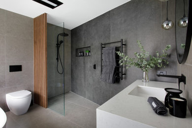 This is an example of a contemporary master wet room bathroom in Brisbane with flat-panel cabinets, medium wood cabinets, a freestanding tub, a one-piece toilet, gray tile, porcelain tile, grey walls, ceramic floors, an undermount sink, engineered quartz benchtops, grey floor, an open shower, white benchtops, a niche, a single vanity and a floating vanity.
